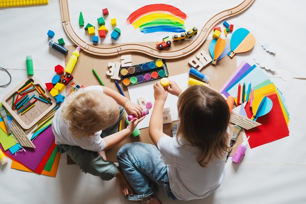 young children painting and playing with educational toys on white paper coveredfloor 