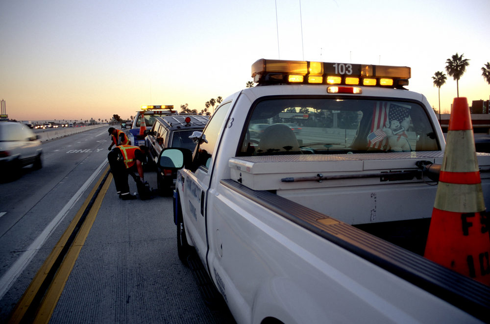 Driver Killed and Two Passengers Hospitalized in Crash on Millerton Rd in Fresno County Municipal roadside assistance helping to tow away a broken car off the freeway at sunset
