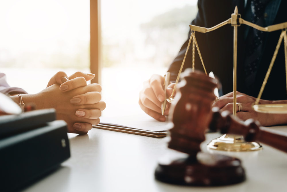 female client with lawyer at desk with scales of justice and gavel with sunlight behind