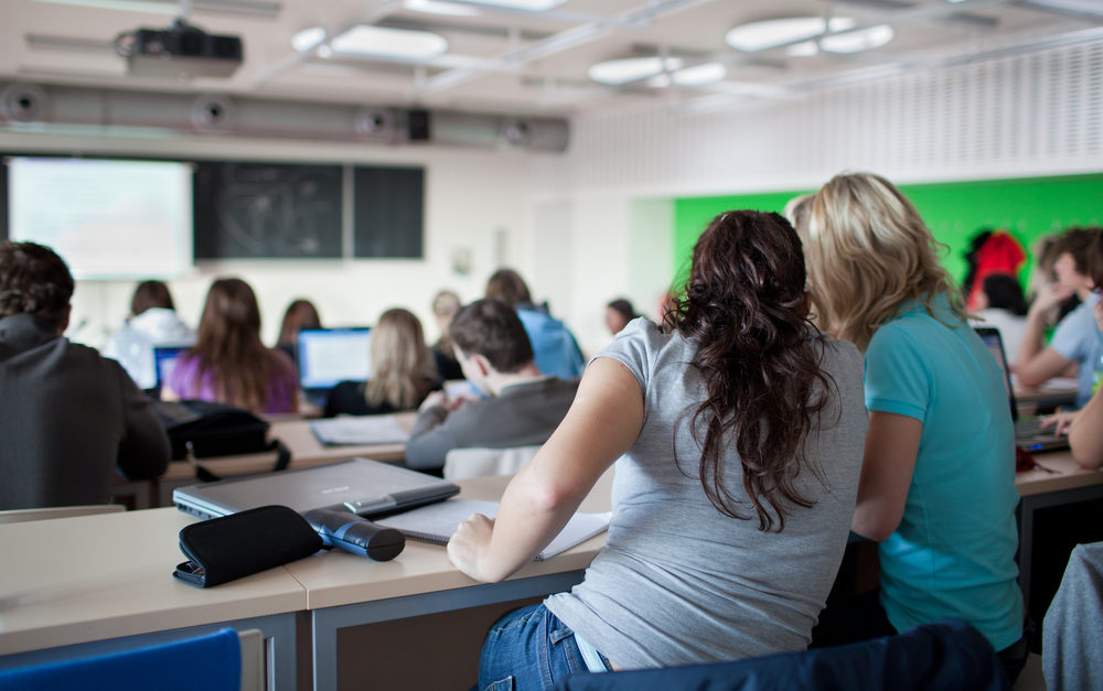 young pretty female college student sitting in a classroom full of students during class