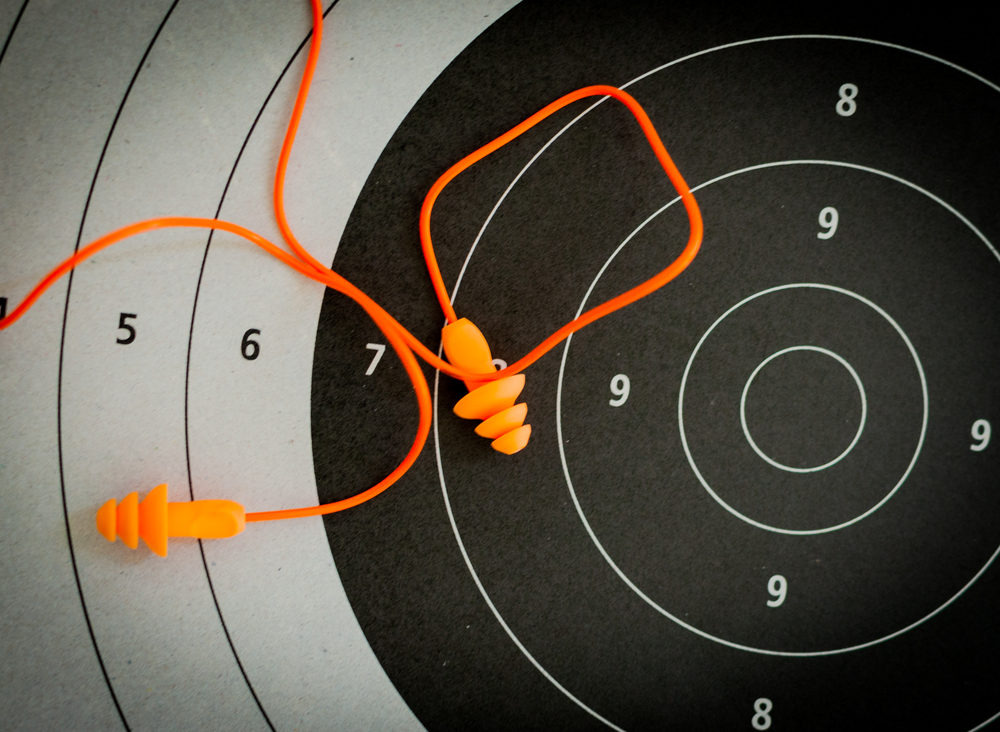 Orange earplugs connected by a cord, resting on a shooting target