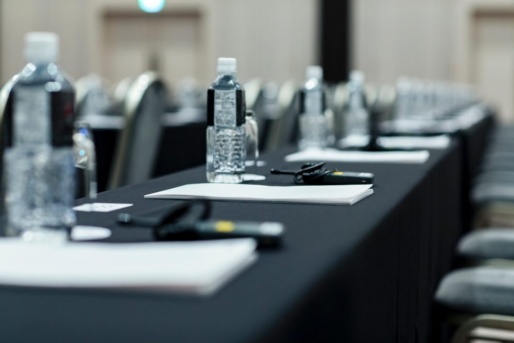 Notepads and water bottles sit on a long, unoccupied desk in a conference room