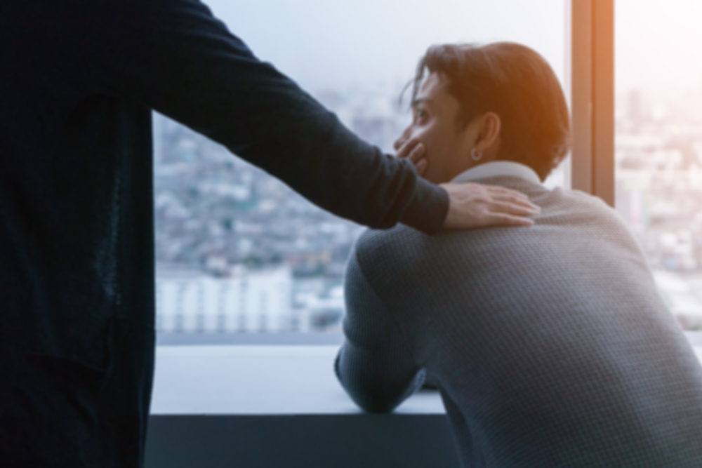 psychologist sitting and touch young depressed asian man for encouragement near window with low light environment