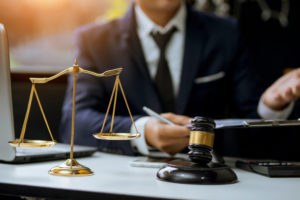 male attorney at desk with a gavel, scales, and a laptop.