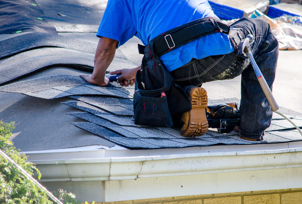 A worker replaces shingles on the roof of a home