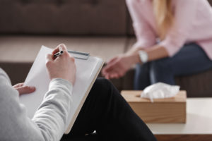 A counselor takes notes while conversing with a woman in his office
