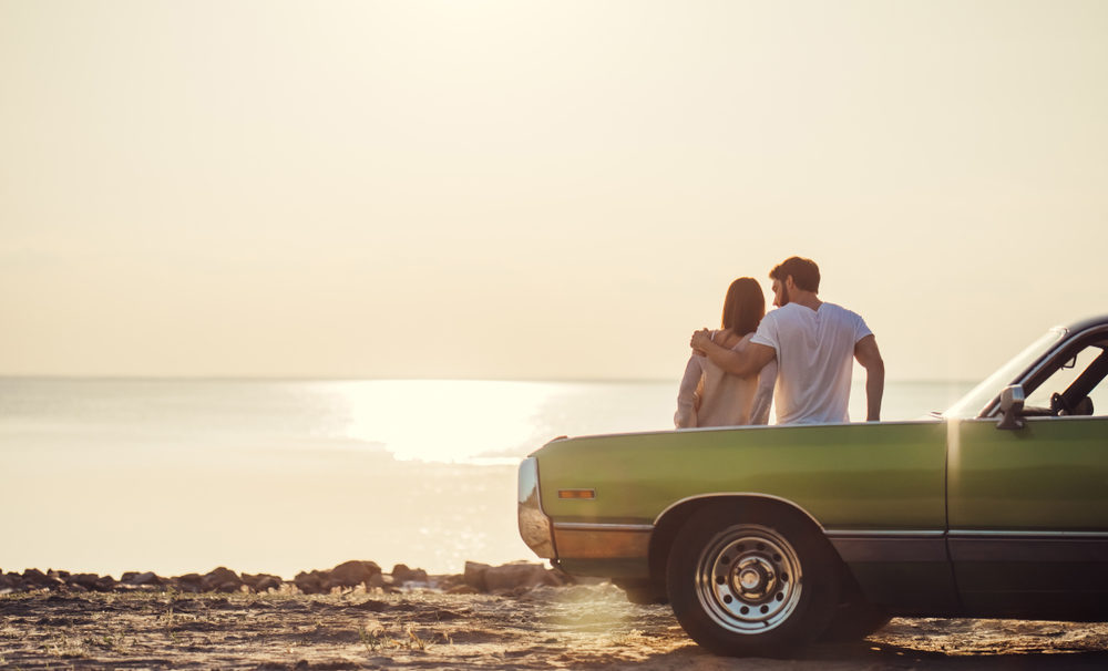 couple is standing near green retro car on the beach