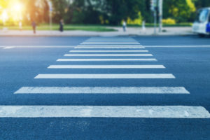 street view of pedestrian crosswalk with sun shining through trees in background