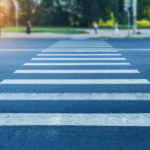 street view of pedestrian crosswalk with sun shining through trees in background