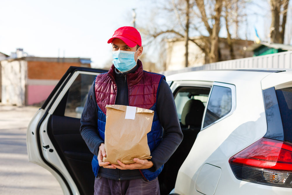 Courier in protective mask and medical gloves delivers takeaway food