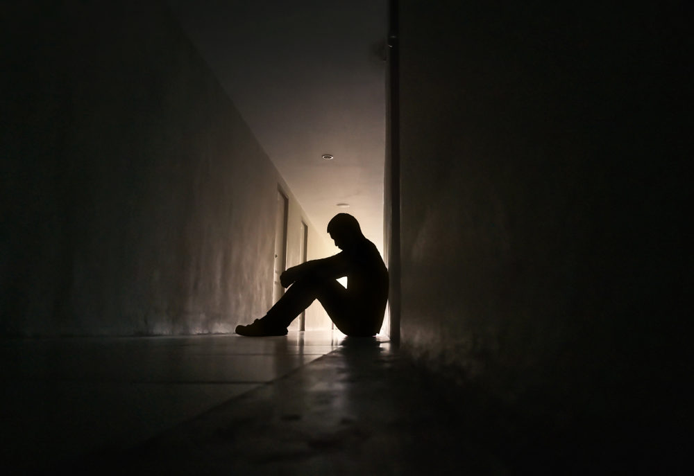 Silhouette of a depressed man sitting in a residential hallway
