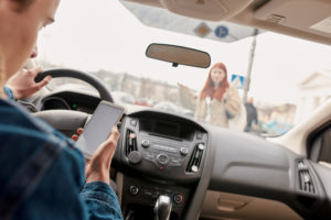 Distracted young male driver looking at the screen of his mobile phone while almost running over a pedestrian.