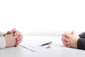 A man and woman's hands on either side of a divorce document, with weddings bands and a pen on the table