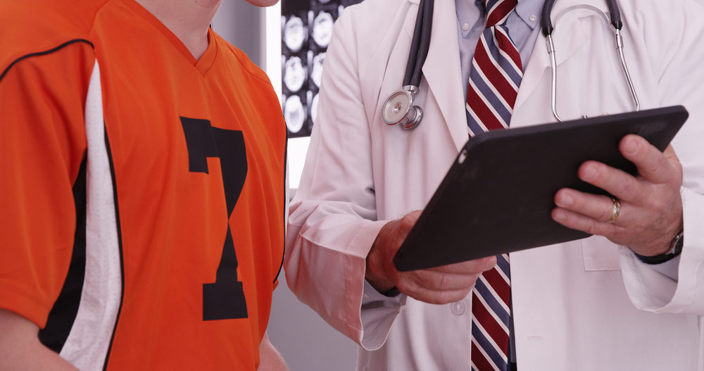 Male doctor looking at tablet with male athlete in office