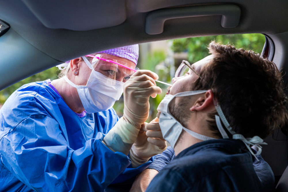 A female doctor in protective suit taking a nasal swab from a man inside a car to test for coronavirus