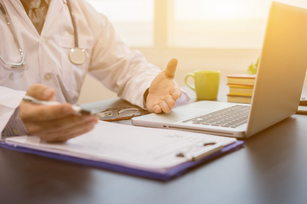 doctor explaining at a desk with a laptop and a chart with sunlight shining through a window