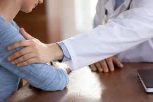 Close up caring doctor therapist touching upset frustrated female patient hand at medical appointment,