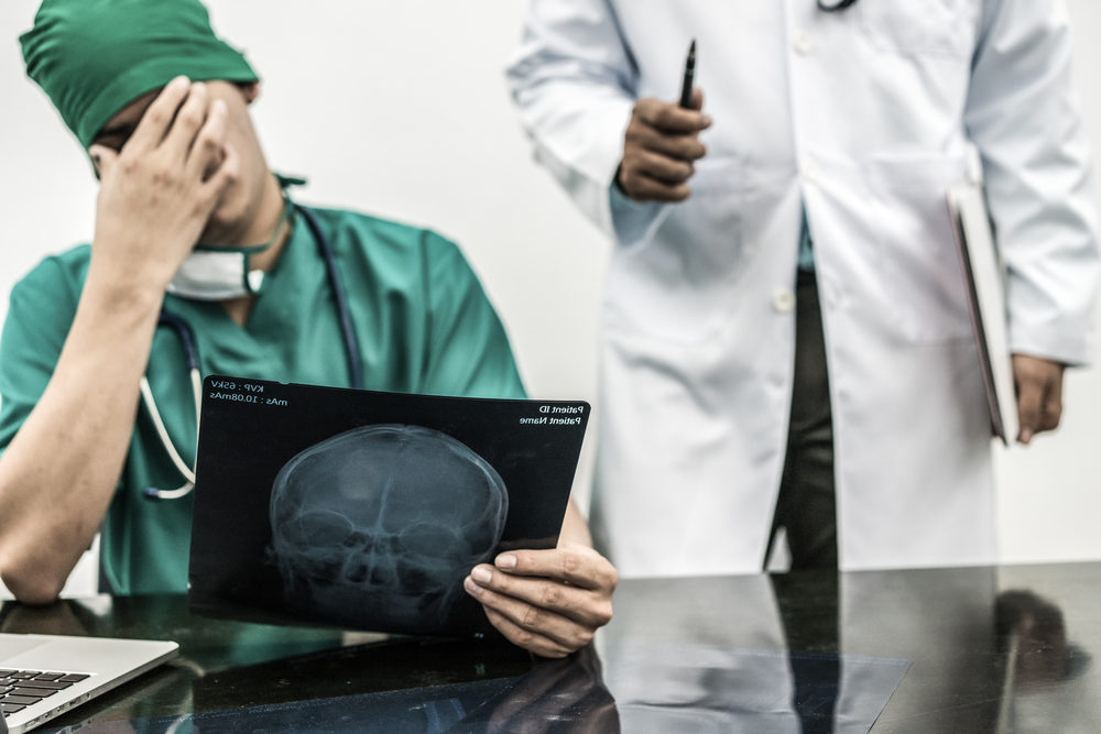 Surgical doctor covering his face with hand expressing disappointment while holding xray film on office desk.