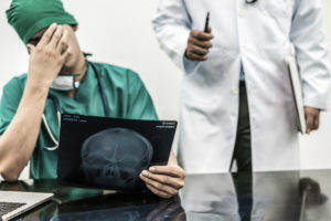 Surgical doctor covering his face with hand expressing disappointment while holding xray film on office desk.