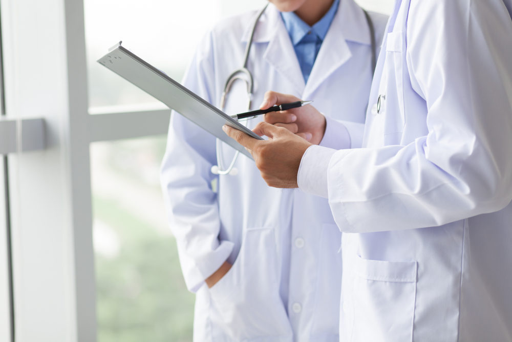 Two doctors in white coats look at a clipboard while talking