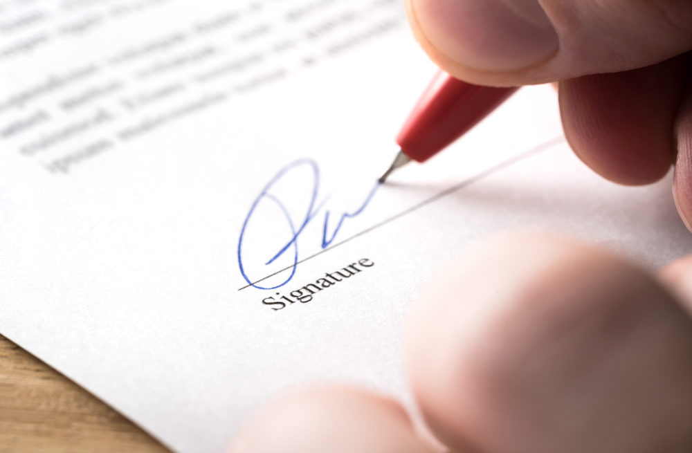 Close-up of somebody signing their name on a signature line