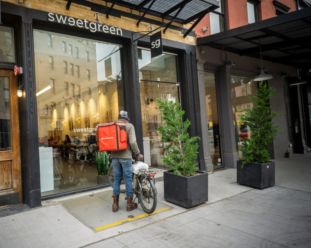 A food delivery driver on bicycle stops by a restaurant to pick up an order 