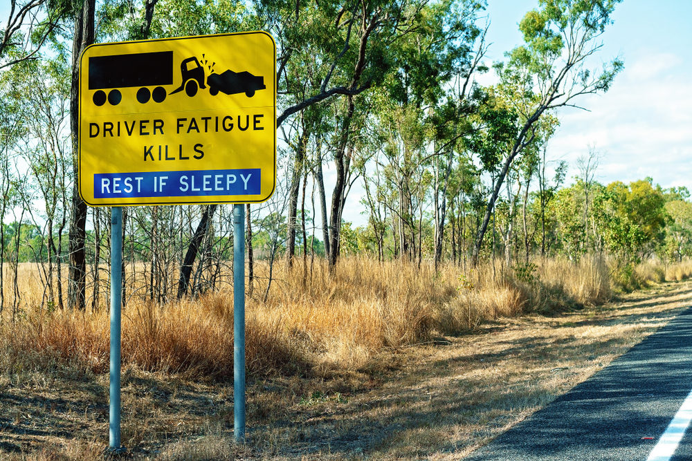 A yellow and black driver fatigue causes crashes alert sign on highway