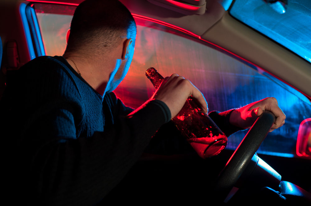  drunk man with alcohol bottle sitting in auto on the background of police car lighting.