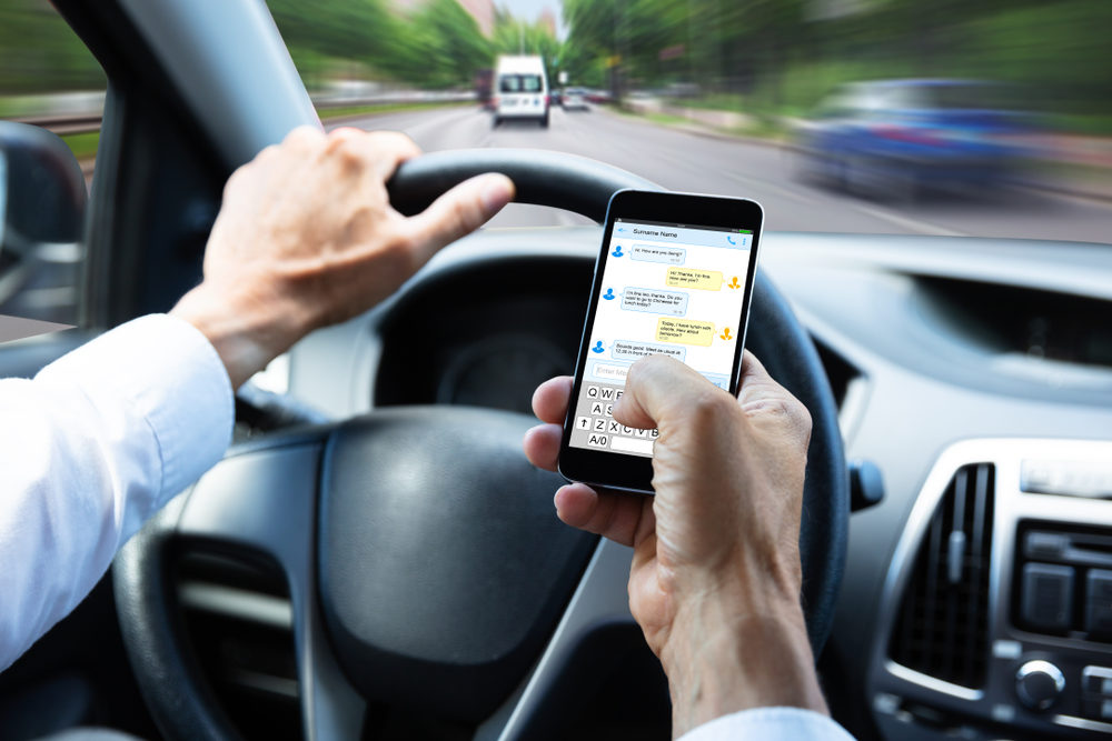 Close-up Of A Man's Hand Typing Text Message On Mobile Phone While Driving Car