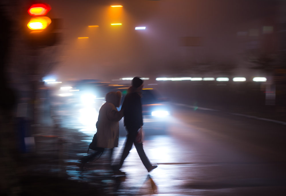 elderly woman pedestrian being assisted crossing the street with motion blur automobiles approaching