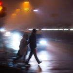 elderly woman pedestrian being assisted crossing the street with motion blur automobiles approaching