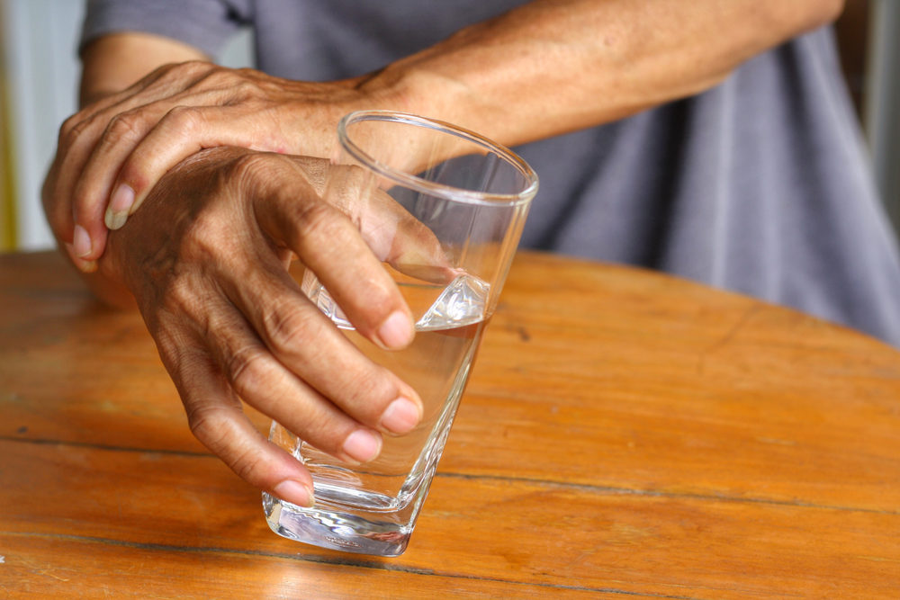 Elderly man is holding his hand while drinking water because Parkinson's disease