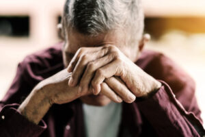 elderly man covering his face with his hands