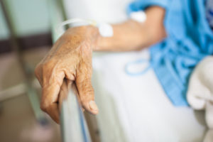 A wrinkled hand grasps the rail of a hospital bed