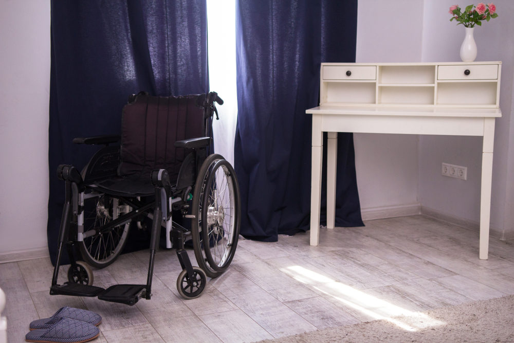 Black wheelchair standing next to window closed with blue curtains.