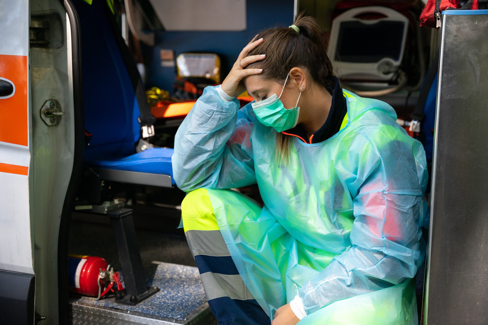Portrait of a young woman doctor sitting on the ambulance resting exhausted where a first aid intervention during the Covid-19 pandemic