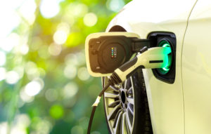EV Car or Electric car at charging station with the power cable supply plugged in on blurred nature with soft light background.
