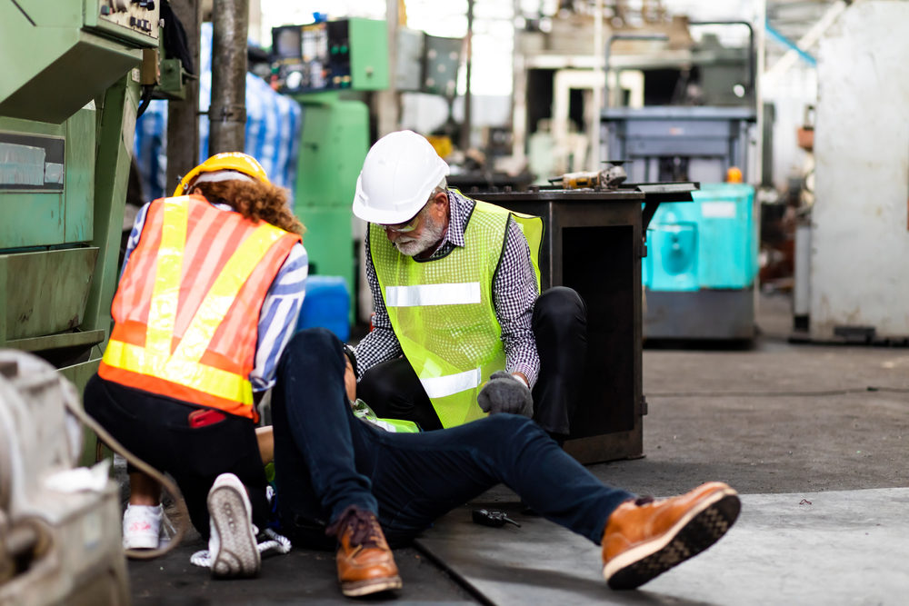 Engineering supervisor talking on walkie talkie communication while his coworker lying unconscious at industrial factory.