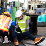 Engineering supervisor talking on walkie talkie communication while his coworker lying unconscious at industrial factory.