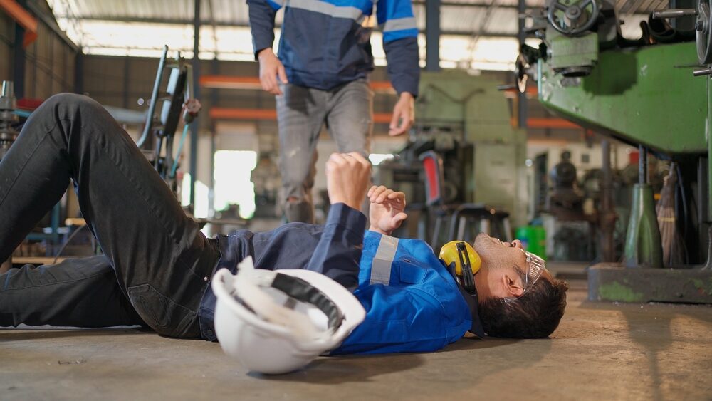 factory worker laying down after injury with a coworker coming to check on him