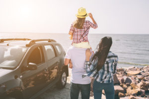 Happy family standing near a car on the beach