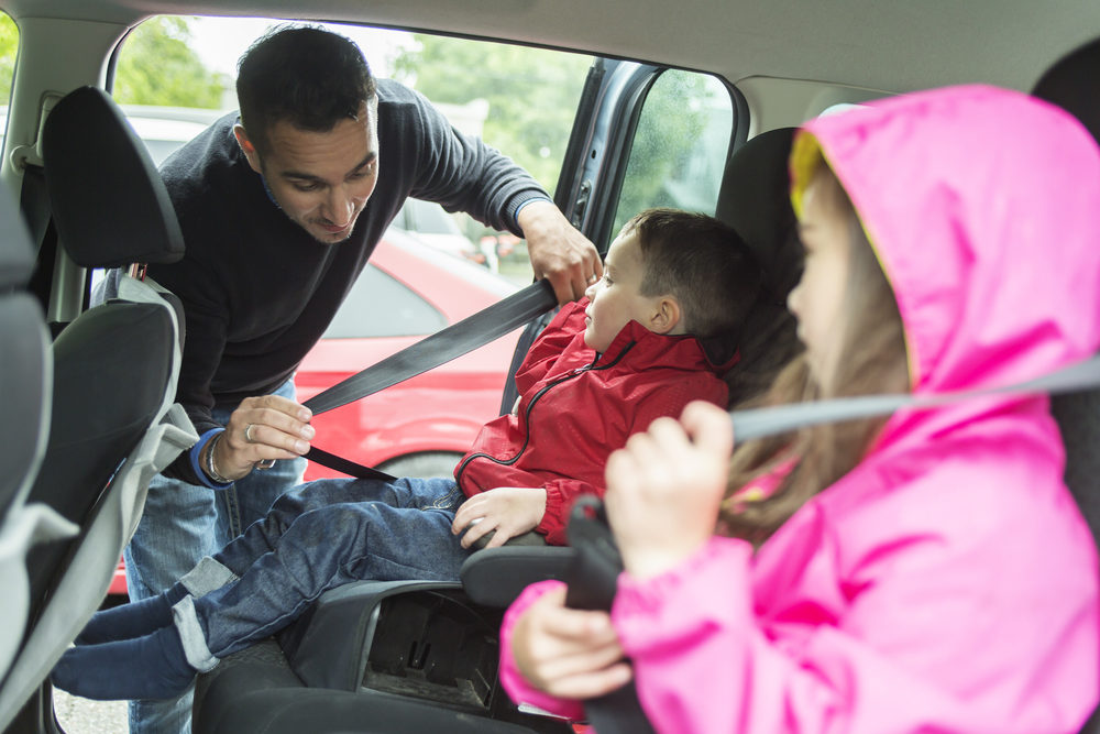 Father putting seat belts on his children