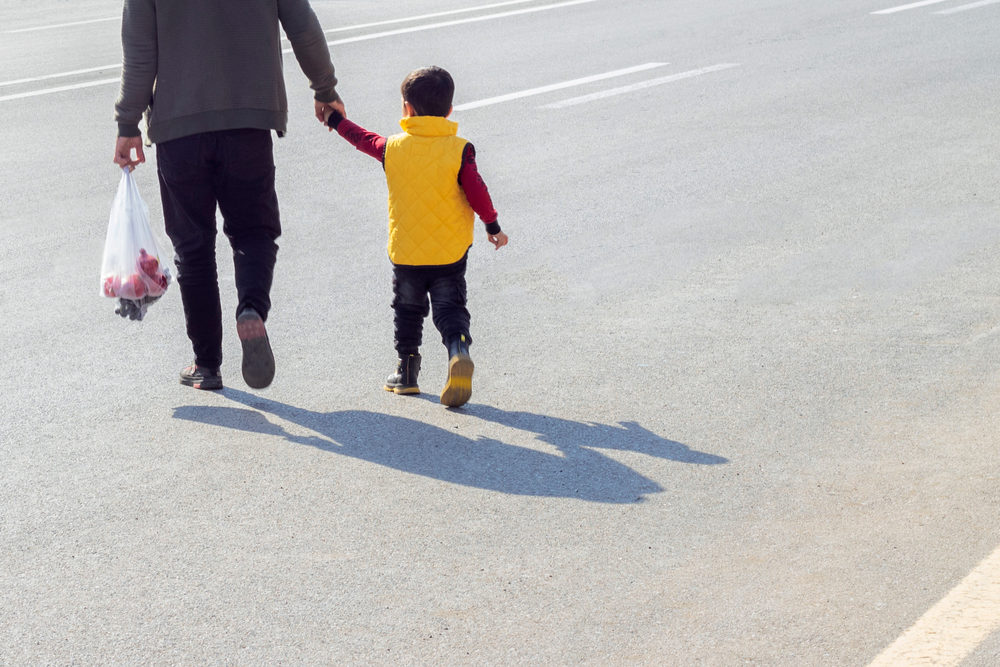 A father holds his son's hand while crossing the road