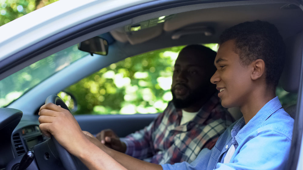 Caring parent teaching son how to drive car, spending time together, family