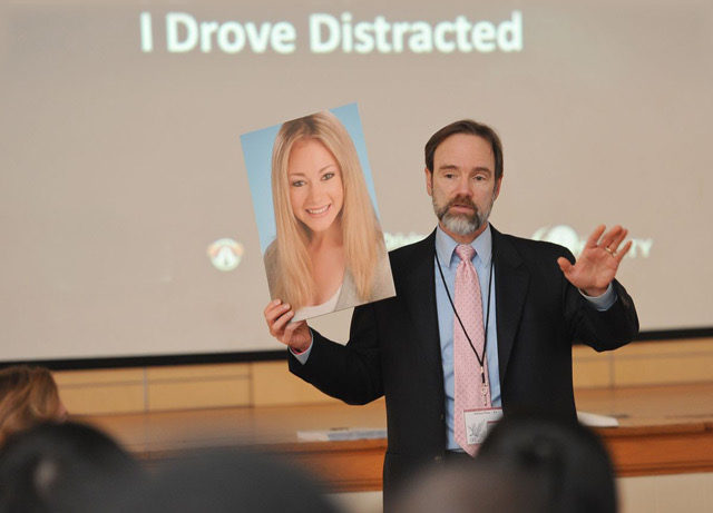 Joel Feldman in auditorium presenting a picture of his daughter Casey at a End Distracted Driving presentation.