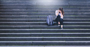 Upset female victim of abuse or harassment sitting on stairs outdoors with backbag