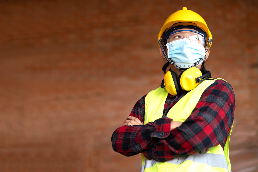 Female construction worker wearing a mask against a wall outside.