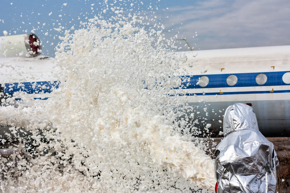A person in protective gear sprays foam on an airplane