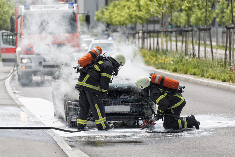 Burning motor vehicle put out by firemen in protective clothing