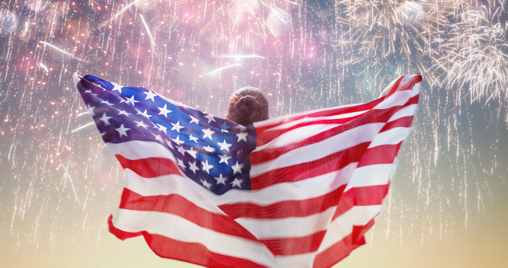 Happy young woman with American flag looking at fireworks.